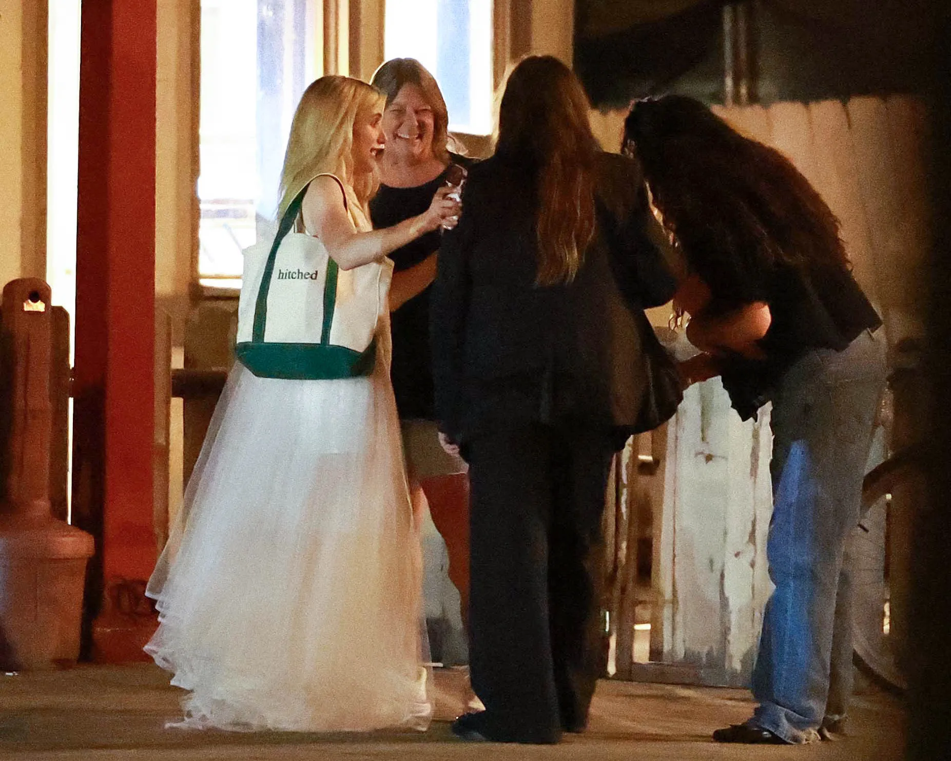 Emma Roberts in a white dress, holding a "hitched" tote bag, bar hopping with friends and family.