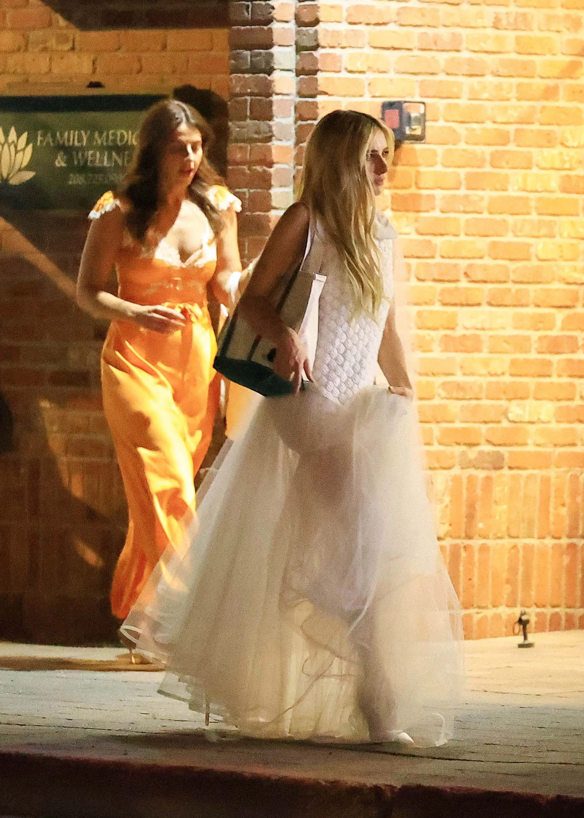 Emma Roberts in a white gown leaving her wedding rehearsal dinner with a companion.