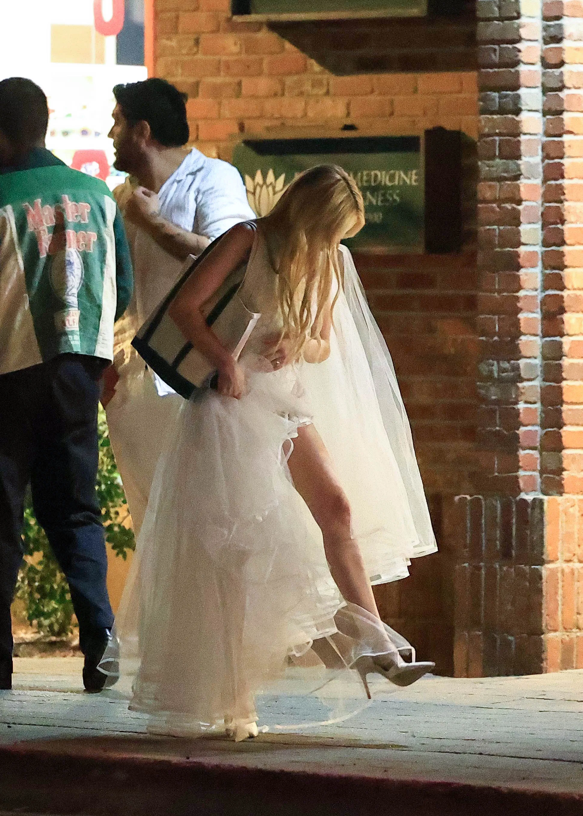 Emma Roberts lifting her white dress to reveal her leg and high heels while walking.