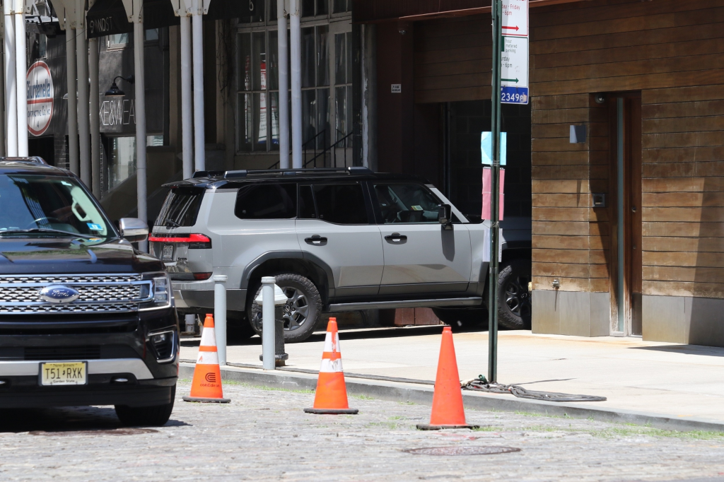 Gigi Hadid's gray vehicle leaving her apartment while a black Ford SUV is parked nearby.