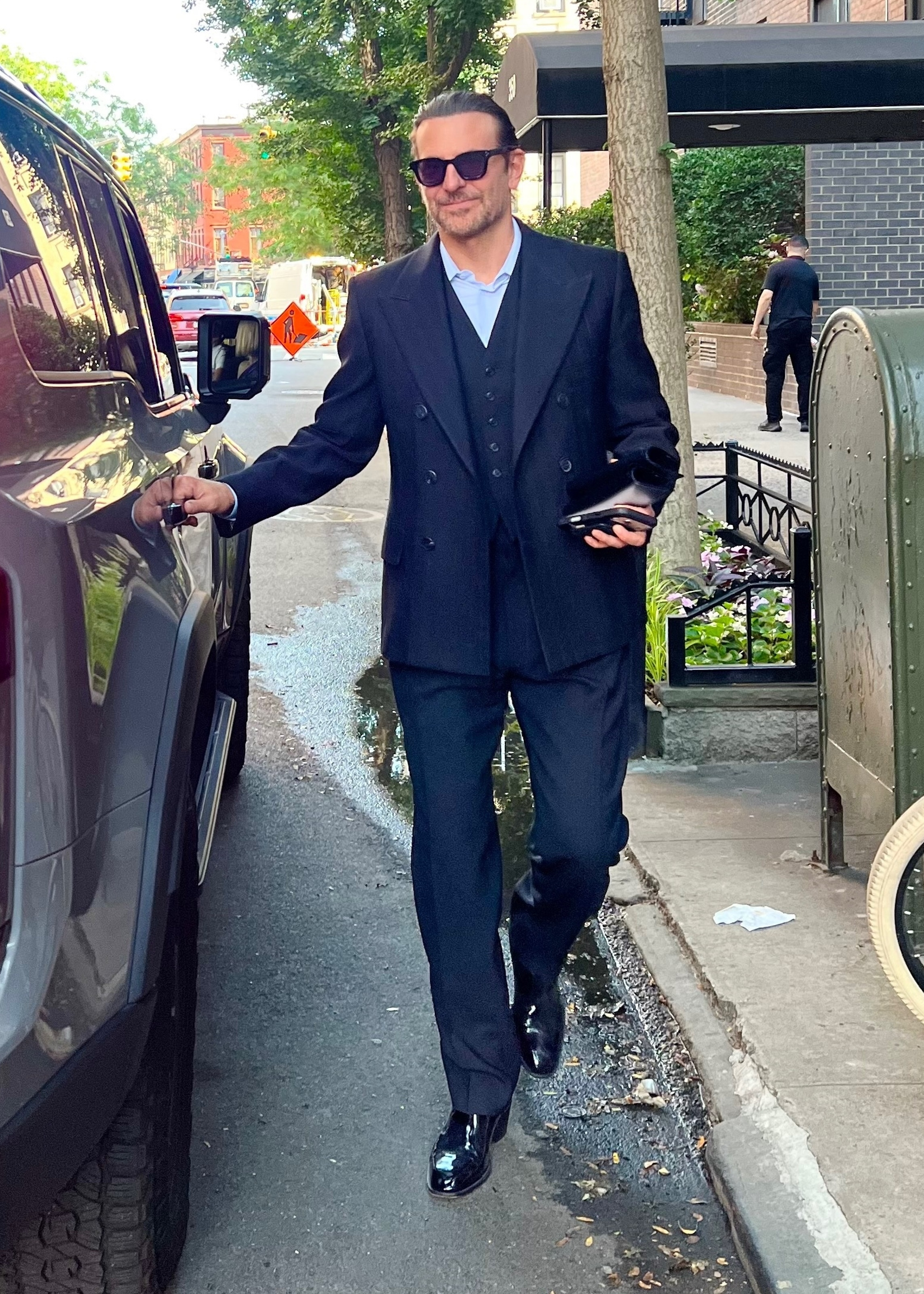 Bradley Cooper in a dark suit with sunglasses getting into a car.