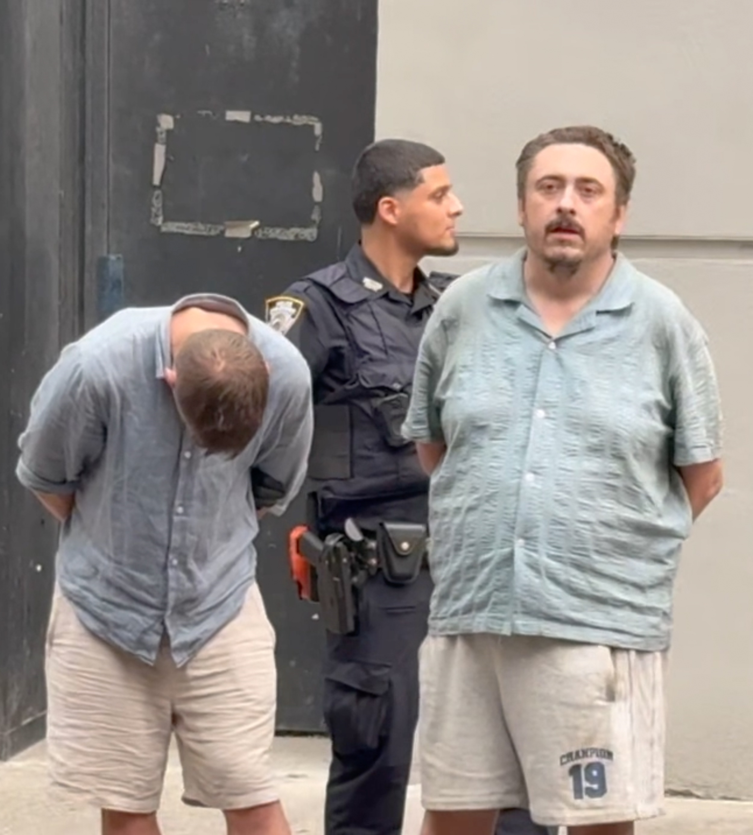 Suspected Today Show intruder Andrew Truelove and another man with their hands behind their backs, standing with an NYPD officer.