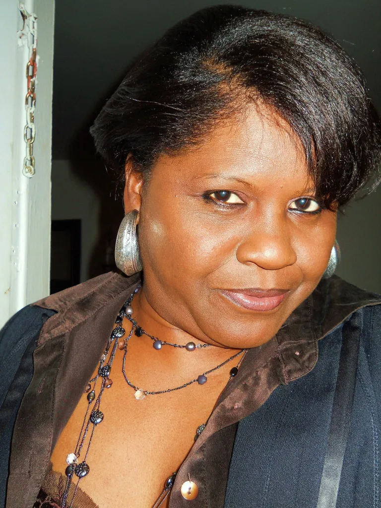 Clemer Ponce with dark hair, large silver hoop earrings, and layered necklaces over a brown shirt.