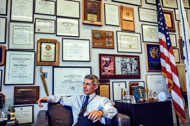 Dr. Fauci sitting in a chair in front of a wall of degrees and certificates.