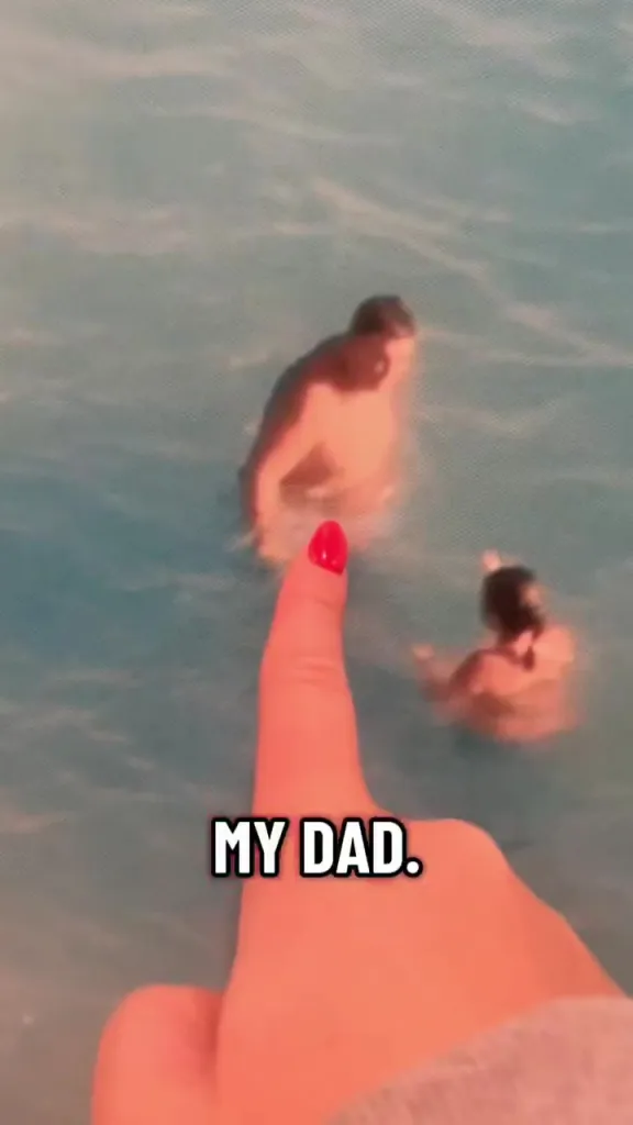 A hand with red nail polish pointing at a photo of a man and a child swimming in blue water.