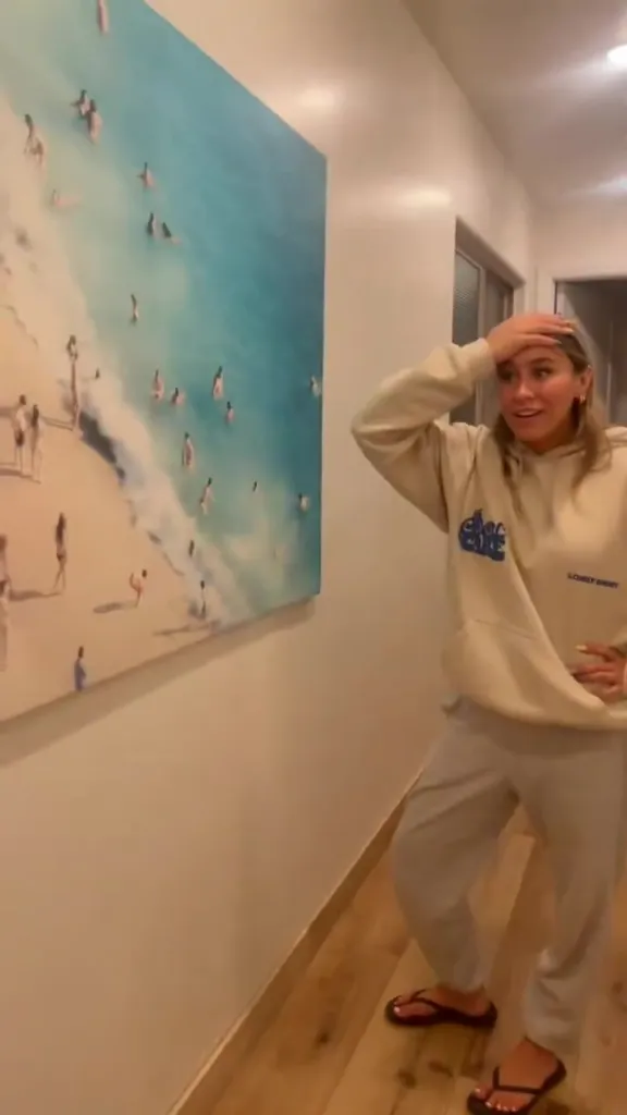 A woman standing next to a large painting of a beach scene.