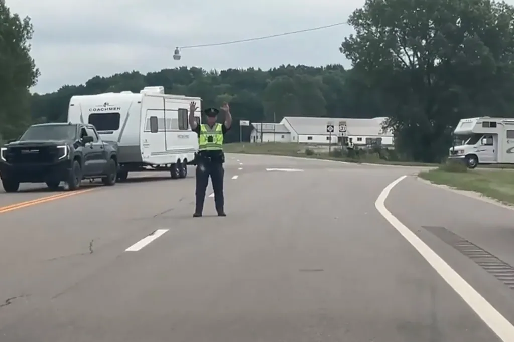 A police officer directs traffic on a road where a truck towing a trailer and other RVs are present.