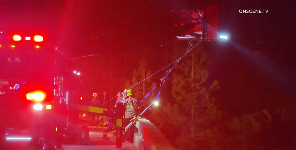Firefighters conduct a rescue operation on a bridge at night.
