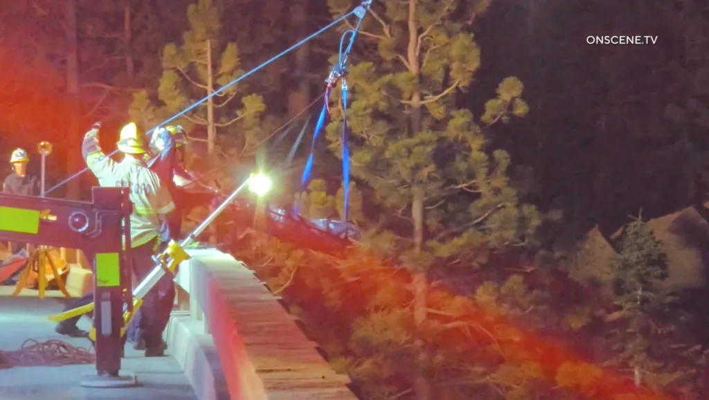 Firefighters use ropes and a stretcher to recover a body from underneath a bridge at night.