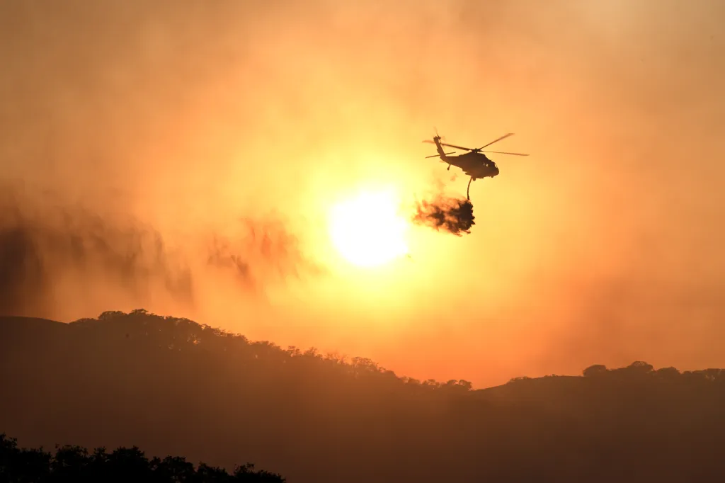 A helicopter drops water on a wildfire during sunset in Sunol, California.