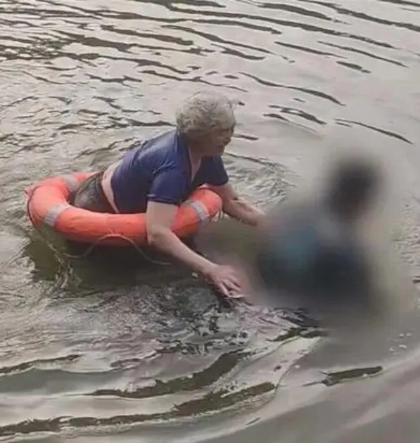 A woman in an orange lifebuoy helping a person in the water.