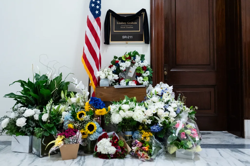 Flowers, wreaths, and an American flag are displayed outside the office of Senator Lindsey Graham.