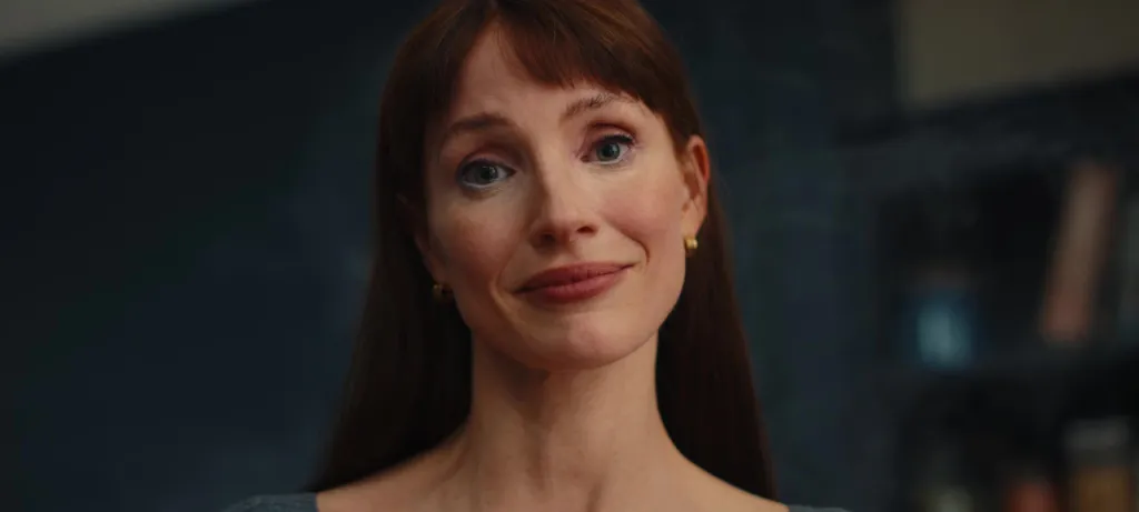 A woman with long red hair and bangs, light blue eyes, and white eyeliner smiles softly.