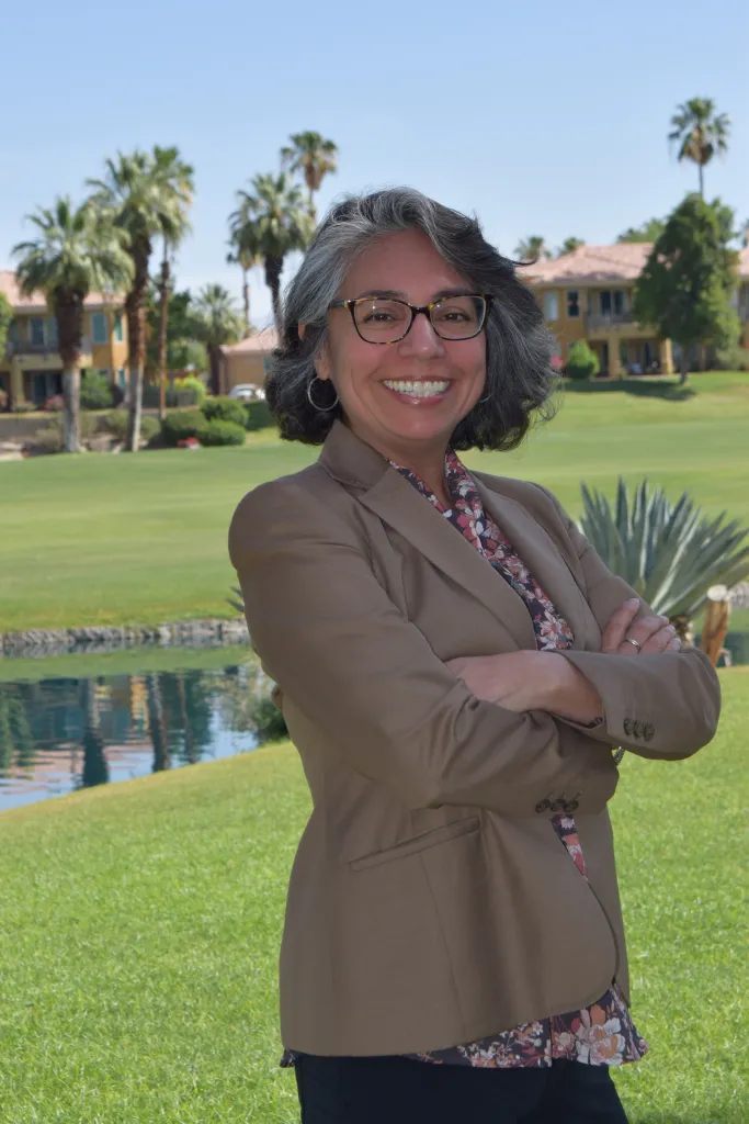 Maria Luisa Palma, former federal and state financial regulator, smiles with arms crossed in front of a golf course.