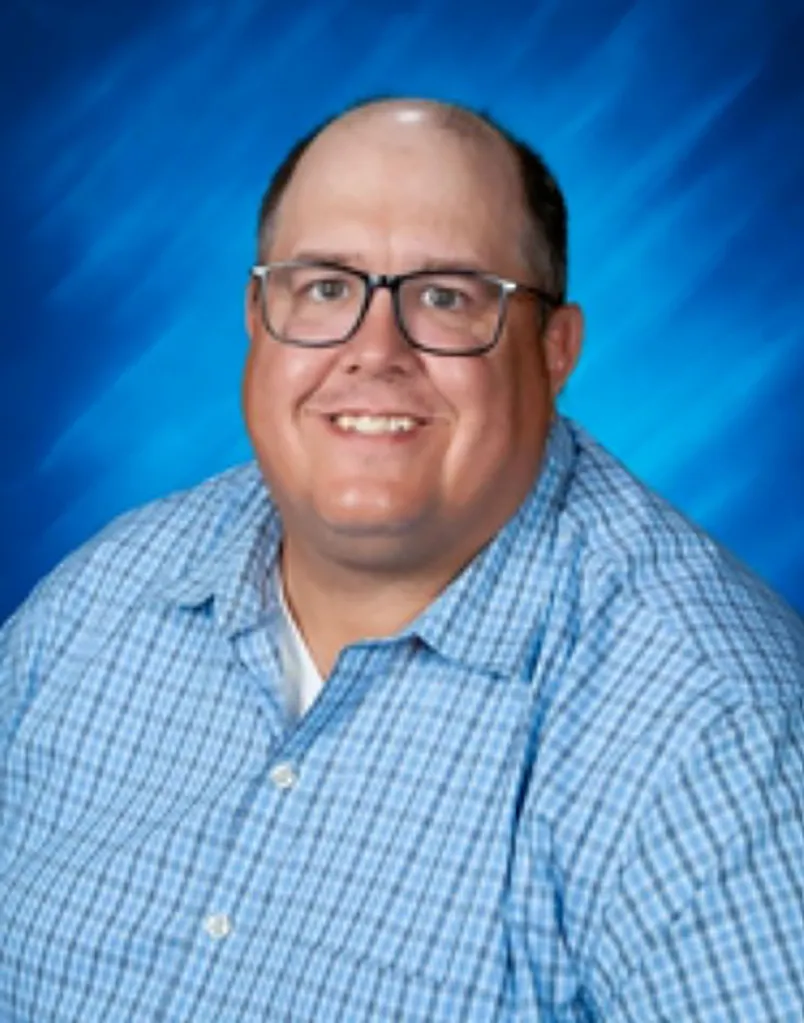 Headshot of Jason L. Rogers, a man with a bald head, glasses, and a checkered blue shirt, smiling at the camera.
