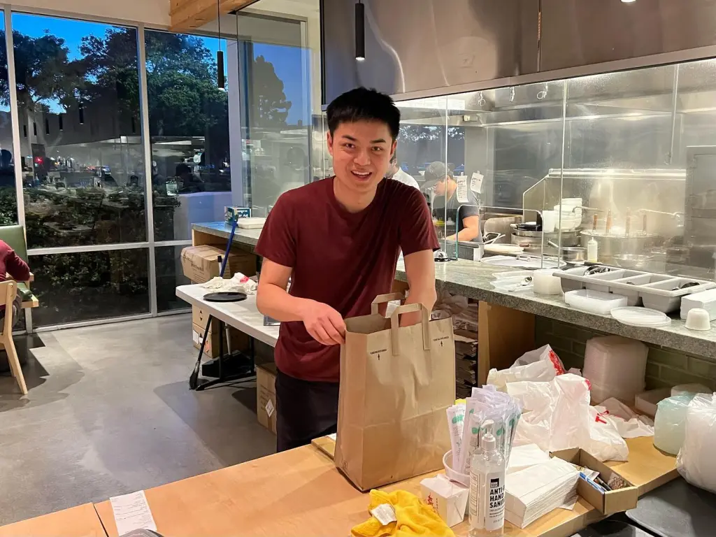 You You Xue holding a brown paper bag in a restaurant.