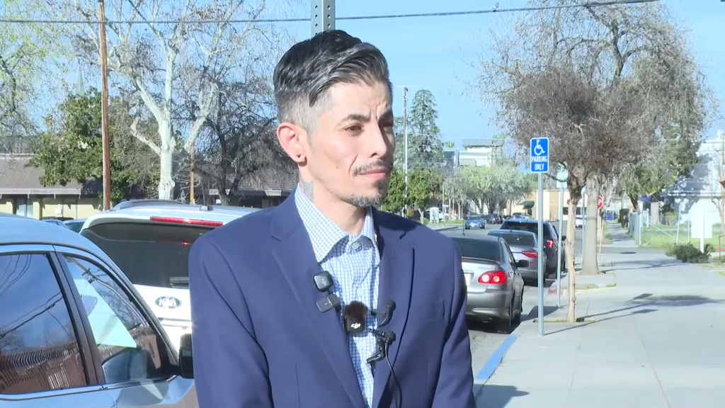 Rene Campos, a registered sex offender, stands outside wearing a suit and multiple microphones while speaking to reporters.