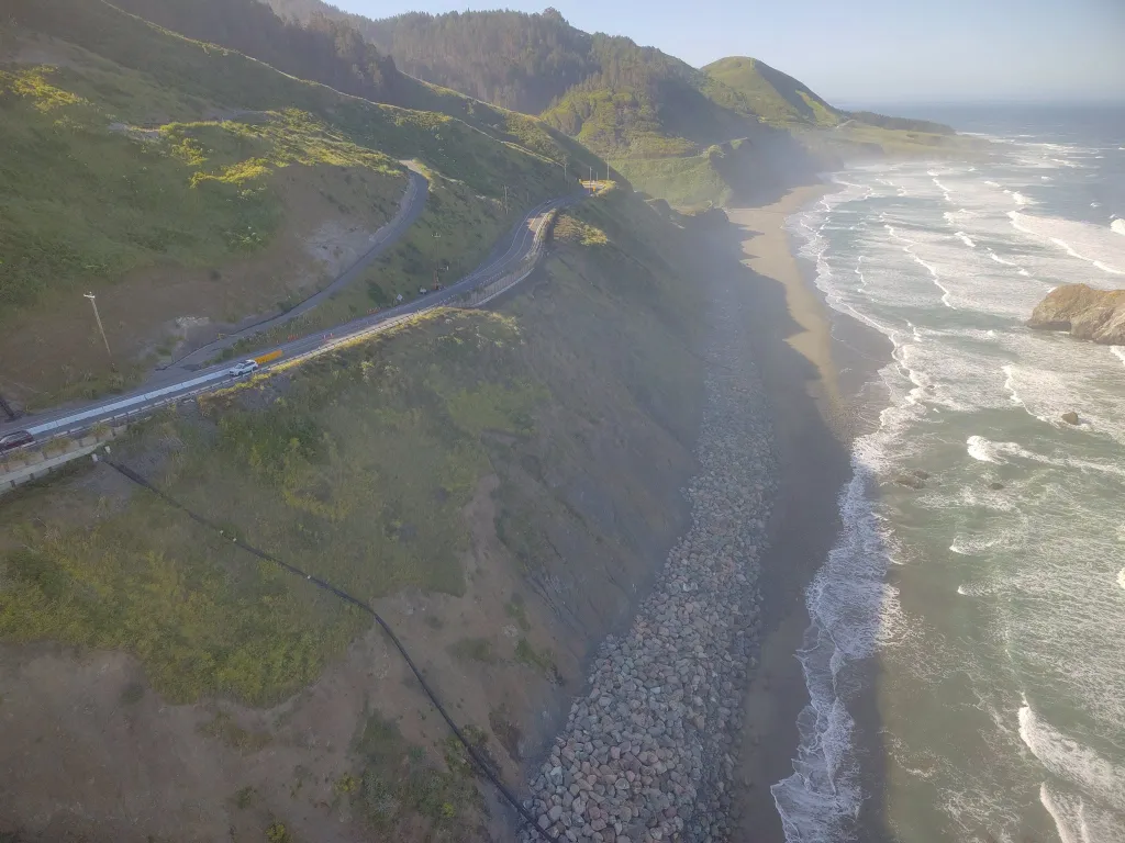 Aerial view of a coastal road winding along a cliff above a beach and the ocean.