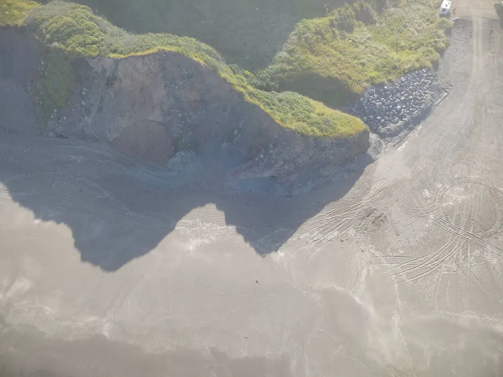 Aerial view of Blues Beach with bluffs, rocks, and tire tracks in the sand.