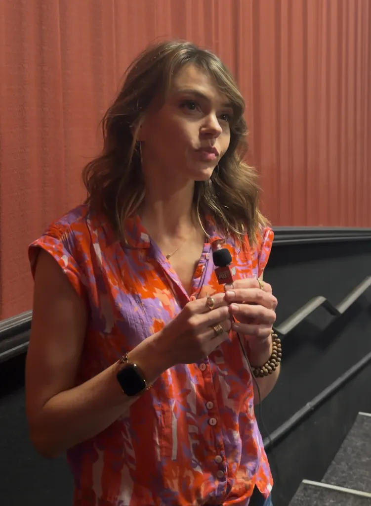Actress Aimee Teegarden holds a microphone from "The Post" against a red curtain background.