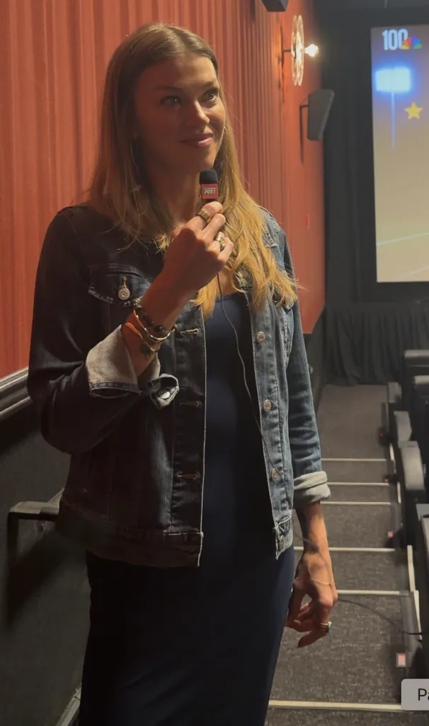 A woman in a denim jacket holds a microphone in a movie theater.