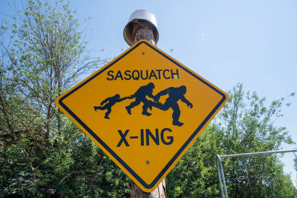Funny yellow sign with a black border, showing three Sasquatch figures running, and the words "SASQUATCH X-ING".