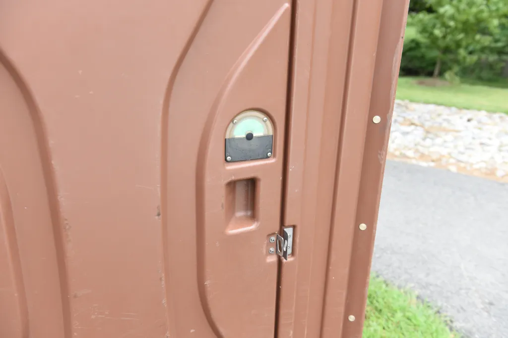 A brown portable toilet with a green/black occupied indicator and metal latch.