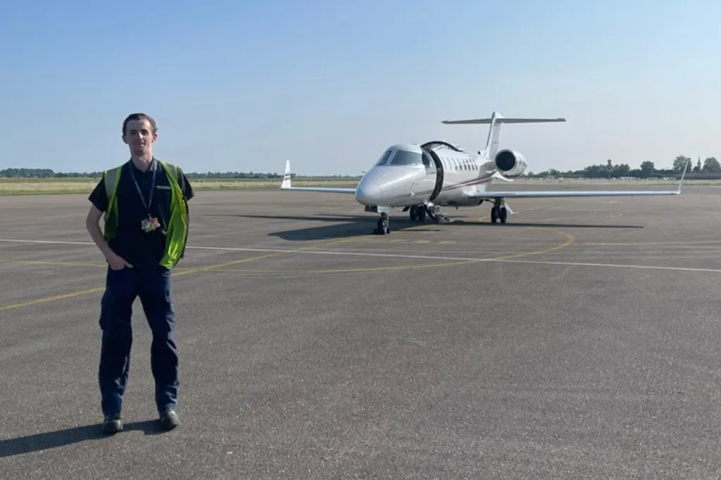 Aircraft technician Georgie Buxton standing on an airfield with a private jet behind him.