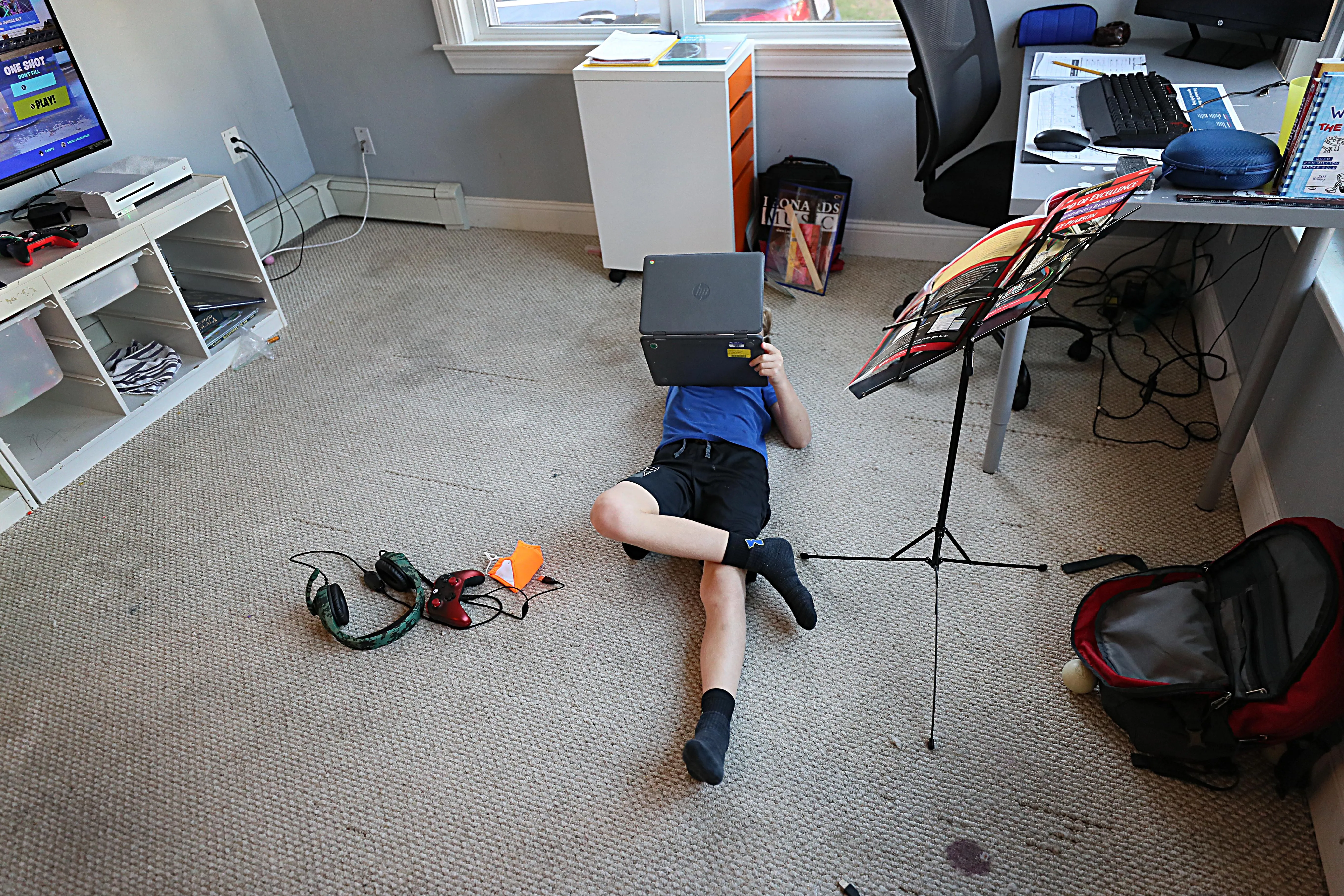 A child lays in a room with a laptop on his stomach and a music stand to his side.