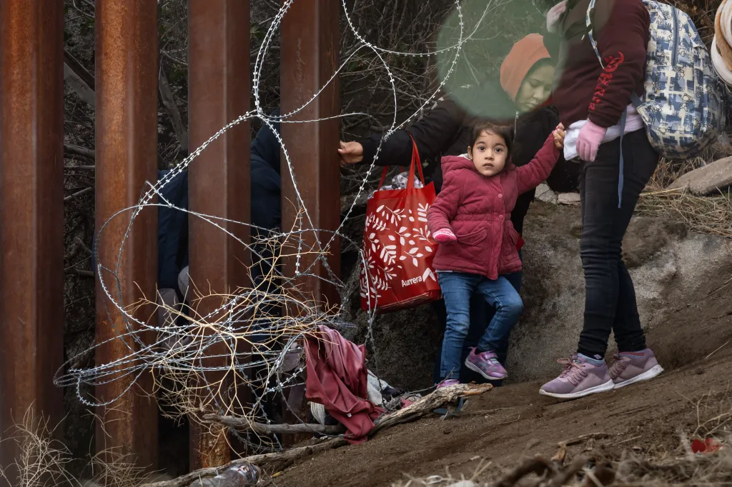 A small child is helped across razor wire at the US-Mexico border.