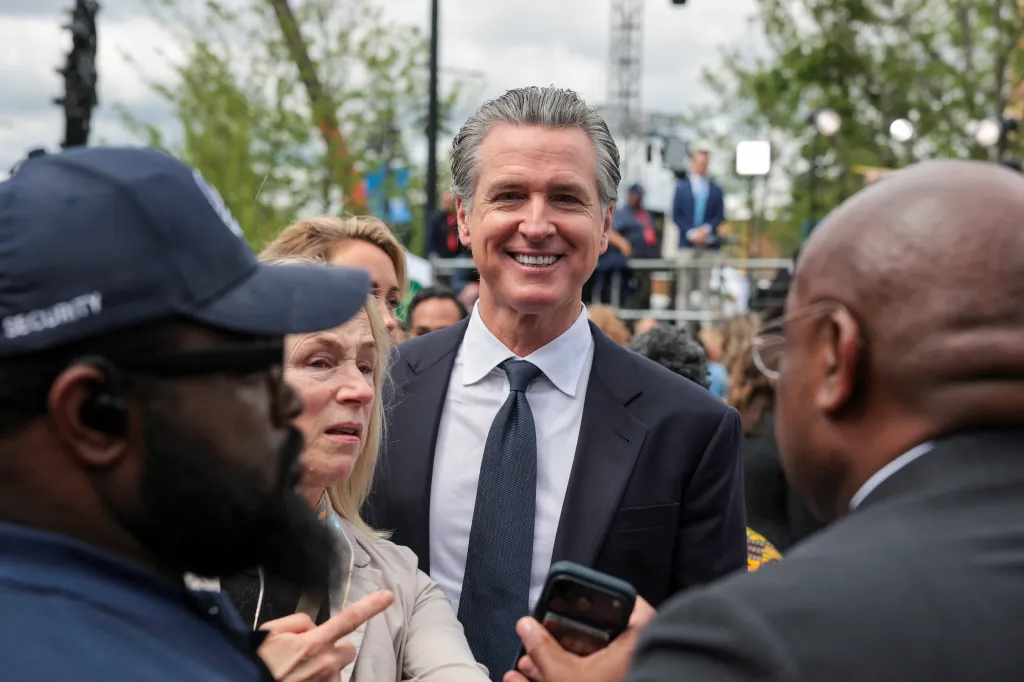 California Governor Gavin Newsom smiling while surrounded by people at the Obama Presidential Center opening.