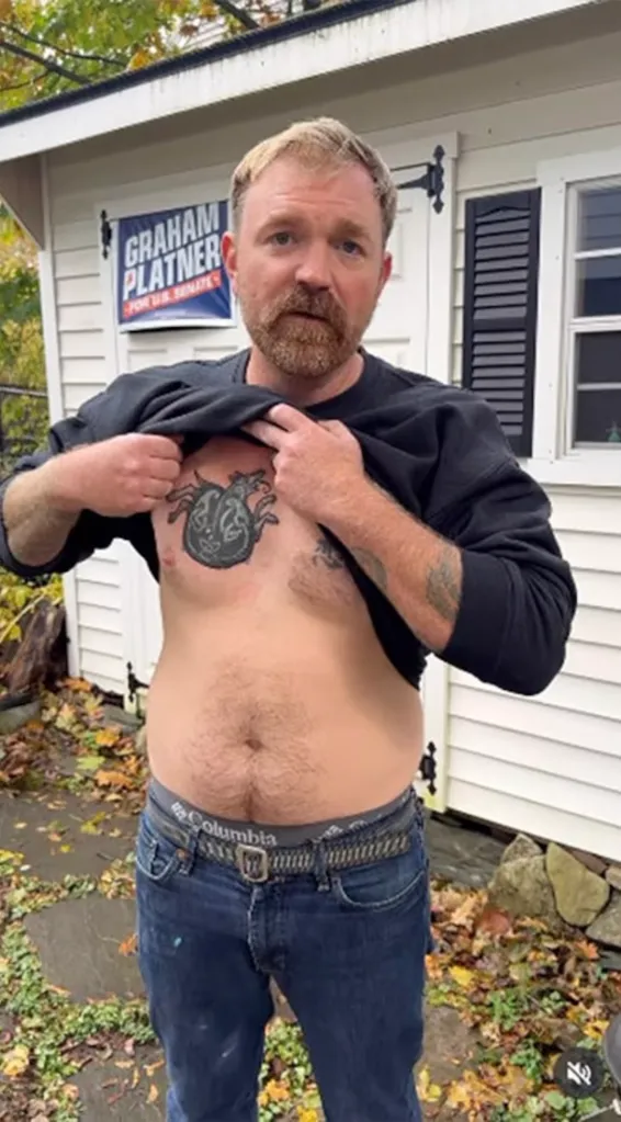 Graham Platner lifting his shirt to show a tattoo on his chest, with a campaign sign in the background.