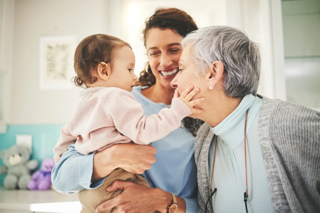 A baby being held by its mother, gently touches the face of its grandmother.