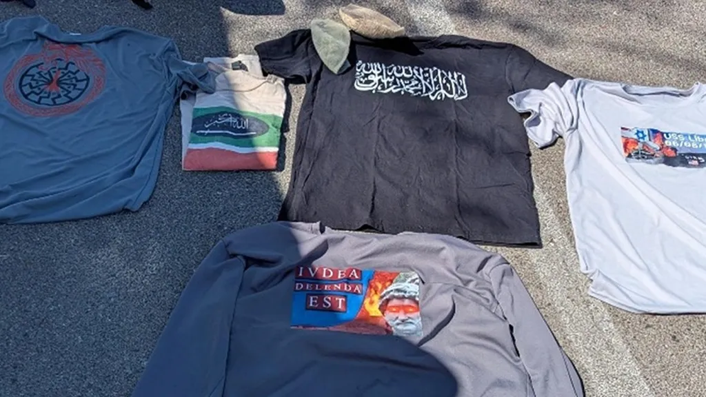 T-shirts with various symbols and text, including Arabic script, the phrase "IVDEA DELENDA EST," and an image related to "USS Liberty 06/08/67."