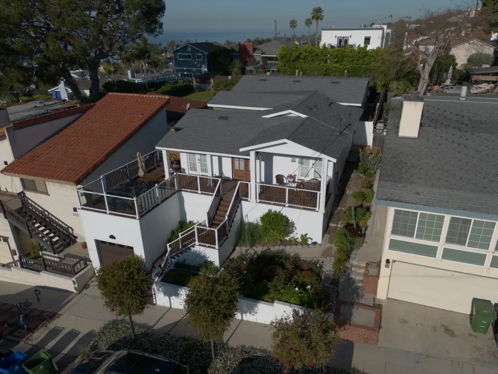 Aerial view of Alberto Carvalho's home, showing a two-story white house with multiple decks, dark roofs, and an ocean view in the background.