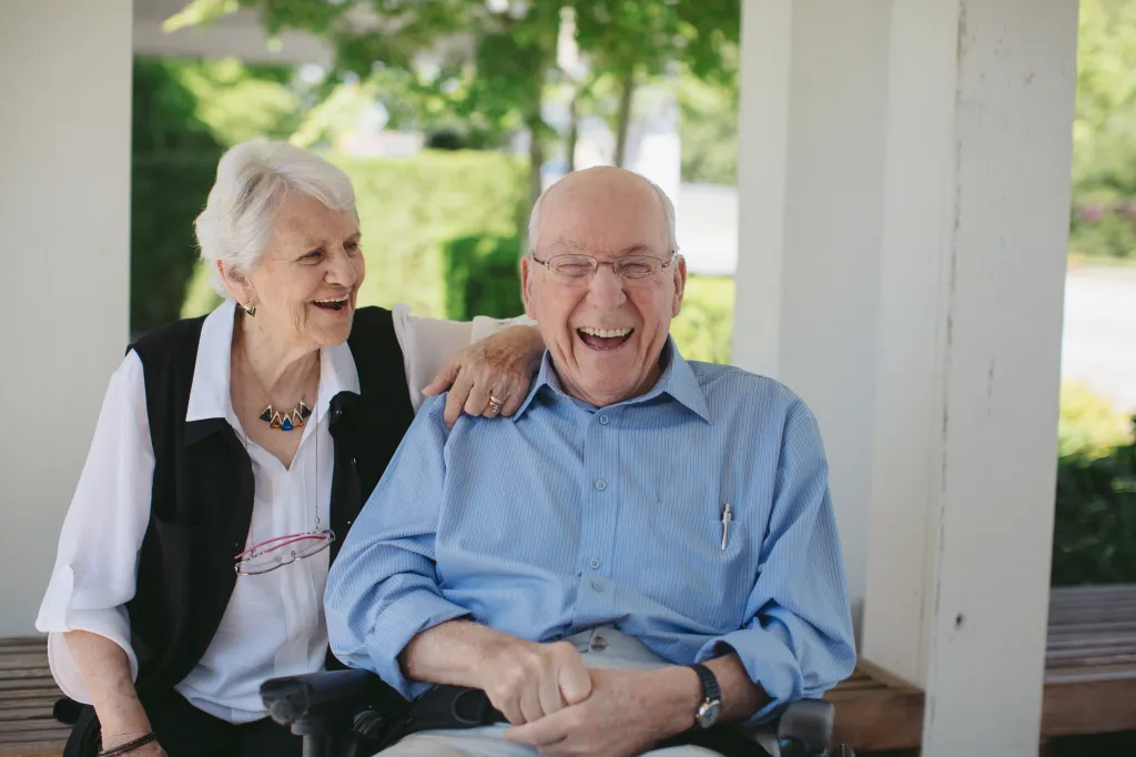 Happy elderly couple, the man in a wheelchair, laughing together outdoors.