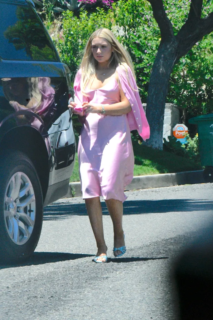 Harper Beckham in a pink dress walks down a street.