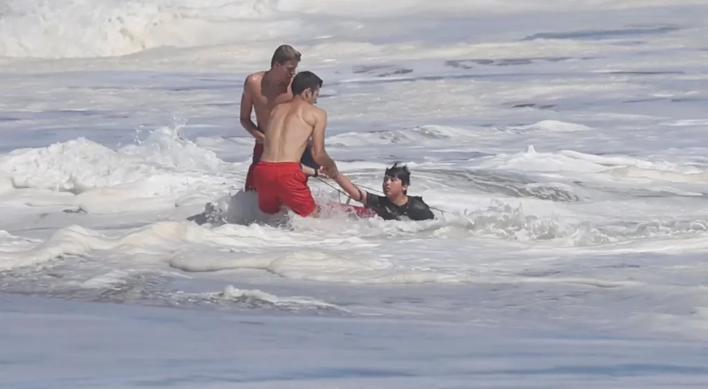 Two lifeguards rescuing a boy from a powerful ocean wave.
