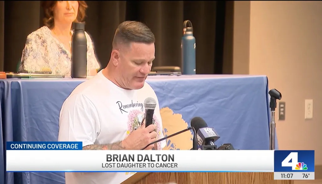 Brian Dalton, who lost his daughter to cancer, speaks into a microphone at a public event.