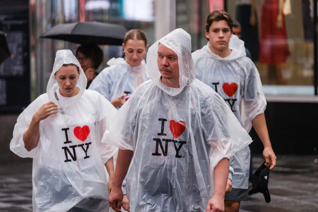 People wearing clear ponchos with "I heart NY" over their clothes, walking in the rain.