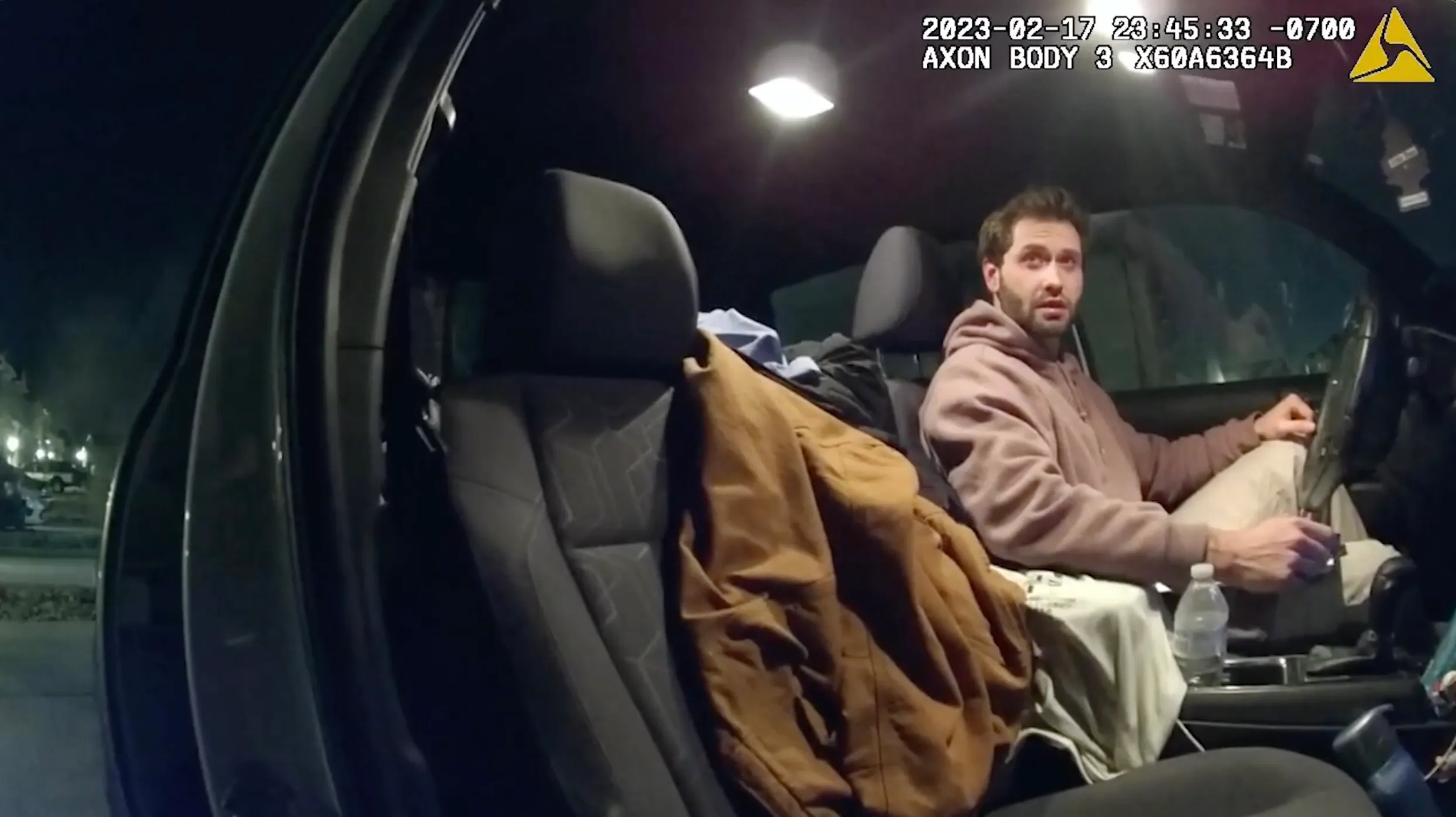 Screenshot from body camera footage showing a man in the driver's seat of a car at night.