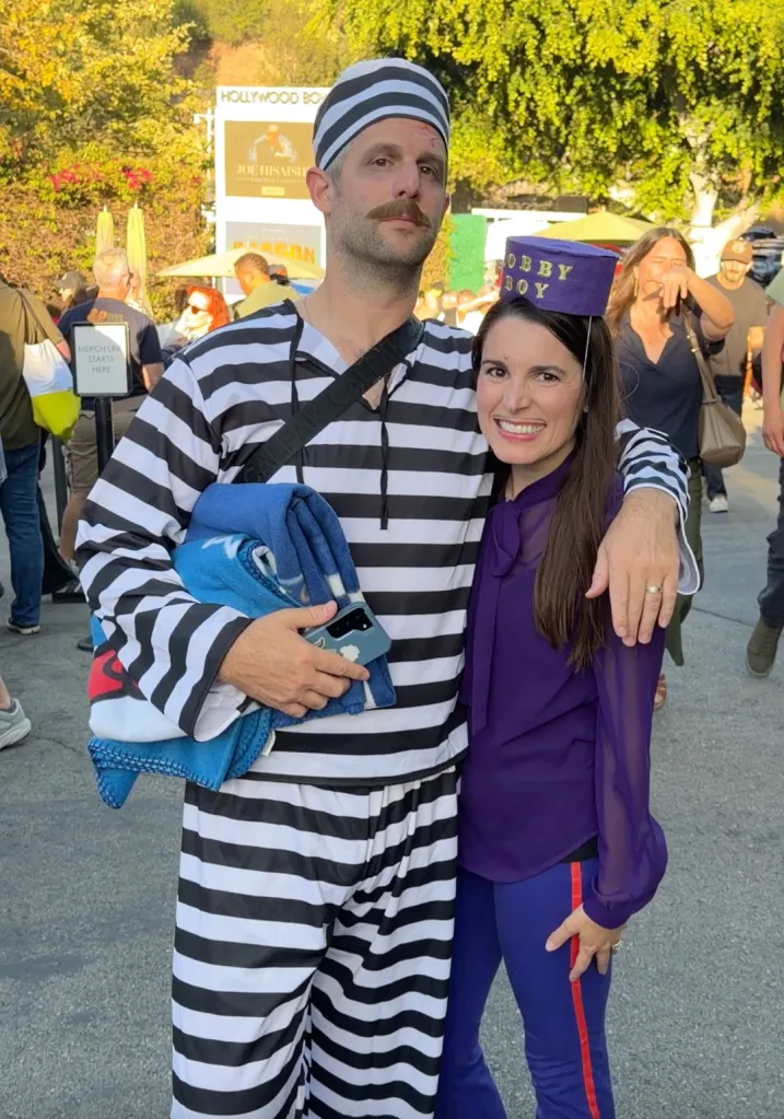 A man in a prisoner costume with his arm around a woman in a purple top and "Bobby Boy" hat at Hollywood Bowl.