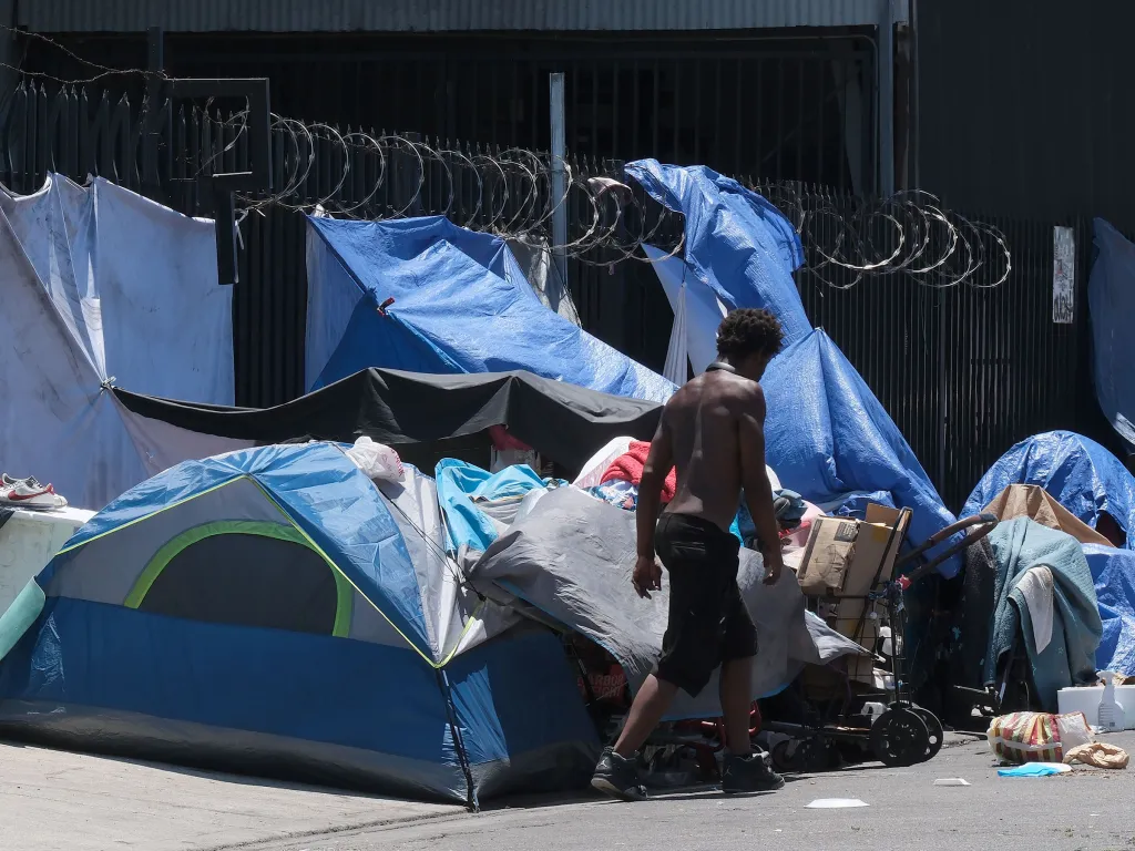 An unhoused man walks past tents and tarps set up on a street in Los Angeles.