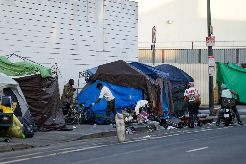 Homeless encampment on a Los Angeles sidewalk with people, tents, bicycles, and shopping carts.