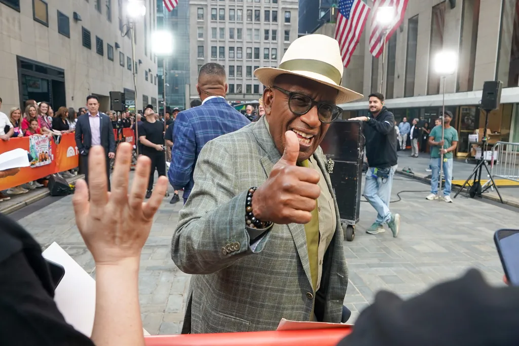 Al Roker, wearing a hat and glasses, smiles and gives a thumbs up to a fan in Rockefeller Plaza.