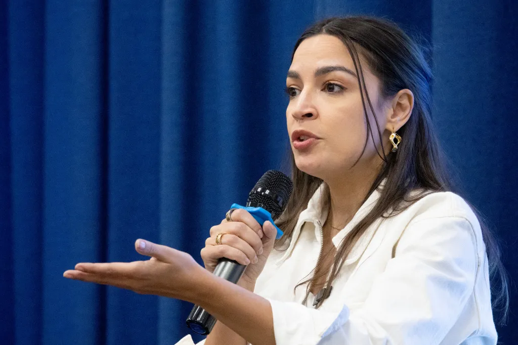 Rep. Alexandria Ocasio-Cortez speaking into a microphone with her left hand open.