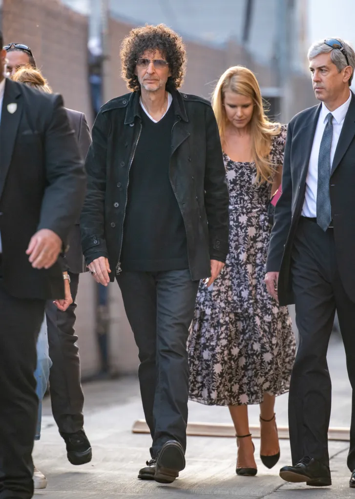 Howard Stern walking outdoors with Beth Ostrosky Stern and security.