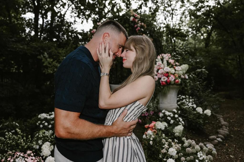 Taylor Swift, in a grey striped dress, and Travis Kelce, in a black top and khakhi pants, embrace, foreheads touching, in a garden.
