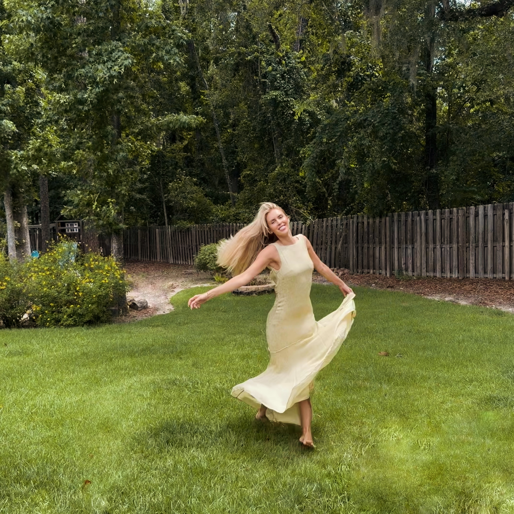 Kayla Rae Reid smiling and spinning in a yellow dress in a backyard.
