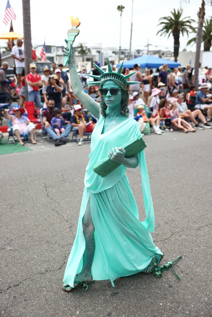 A person dressed as the Statue of Liberty walks in a parade.